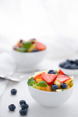 Fresh fruit salad with fresh strawberries, kiwi, apricots and blueberries, decorated with leaves of fresh mint in white plates on a white table