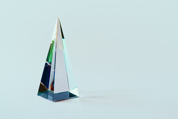 Glass pyramid prism on pastel light background with colorful sunlight reflection with copy space, horizontal