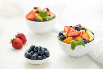 Fresh fruit salad with fresh strawberries, kiwi, apricots and blueberries, decorated with leaves of fresh mint in white plates on a white table