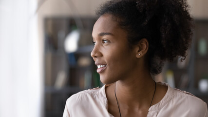 Head shot close up of smiling dreamy African American woman looking to aside, pensive attractive...