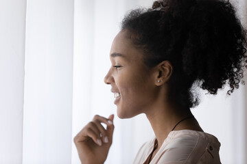 Head shot profile of smiling dreamy African American woman looking to aside in window, happy young female thinking, visualizing good future, dreaming about opportunities, planning starting new day
