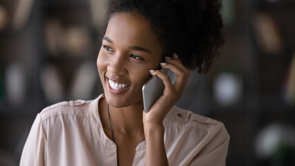 Head shot of smiling African American woman talking on cellphone, enjoying pleasant conversation with friend or boyfriend, close up happy young female holding smartphone, chatting, making phone call