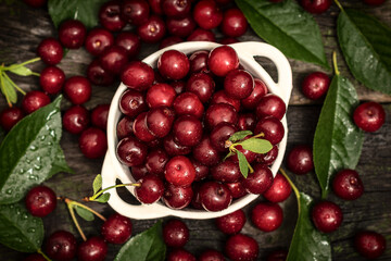 Fresh sweet cherries bowl with leaves on wooden desktop table. water drops on Fresh sour cherry berries
