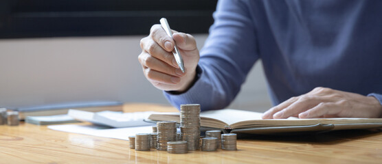 Man counts the coins piled up on the table in preparation to save money, Take note of household financial expenses, Saving money for future growth and knowing how to manage your spending wisely.