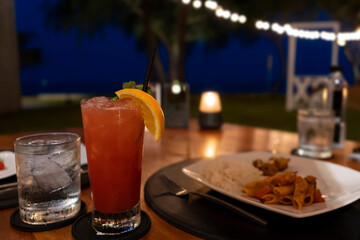 A glass of cocktail and dinner food from the beach bar in hotel with a beautiful night view in the background