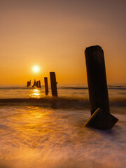 Sea waves and logs standing in front Orange sunset in the evening. Beautiful nature in Thailand.