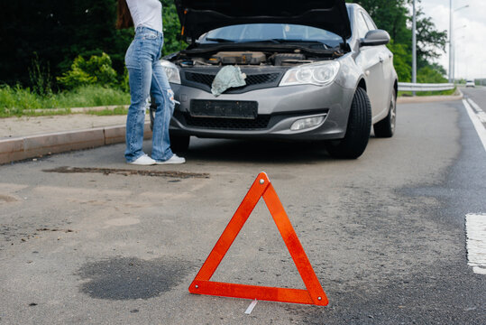 A young girl stands near a broken-down car in the middle of the highway and looks under the hood. Failure and breakdown of the car. Waiting for help.