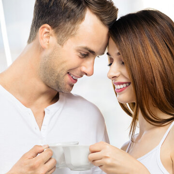 Image of smiling happy amazed couple with cups of some drinks at home. Portrait of standing close and looking at each other models in love family concept. Man and woman posing together. Square.