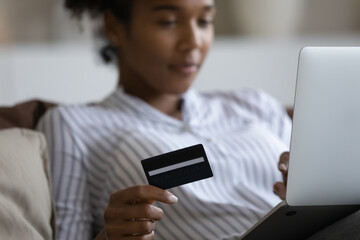 Close up cropped of African American woman paying online by credit card, using laptop, young female customer shopping, browsing internet banking service, checking balance, making secure payment