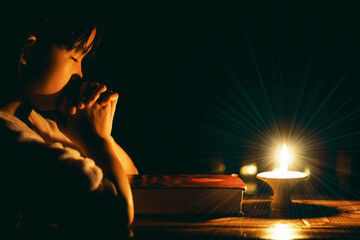 Child praying to God with lighting candle at night time.Spirituality and religion, Religious...