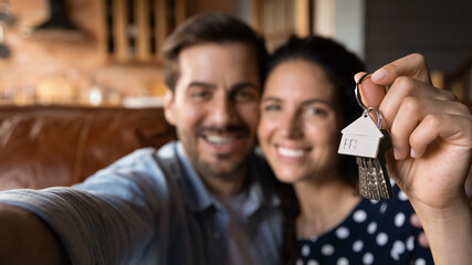 Happy young husband and wife showing key at camera, taking selfie. Property buyers, tenants...