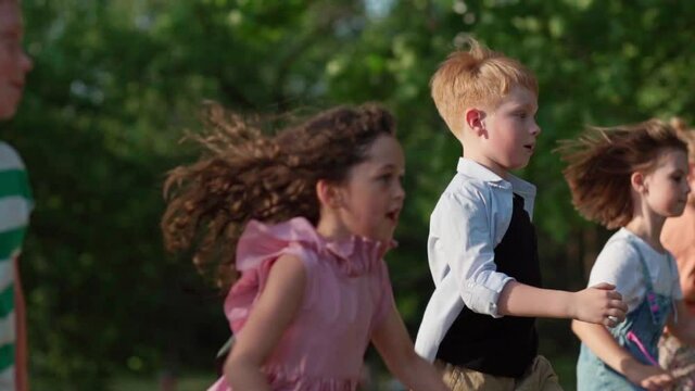 Side view of active kids running in park in slow motion. Children having fun attempting to run faster than friends. Group of carefree little friend playing together