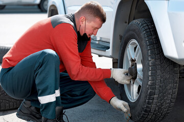 A man changes a wheel on a car on the street on a sunny day. Help on the road with a tire puncture.