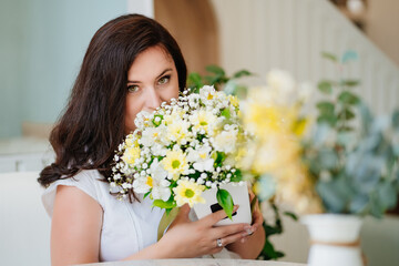 Naklejka premium attractive woman in white clothes with flowers at the table in a light room. 