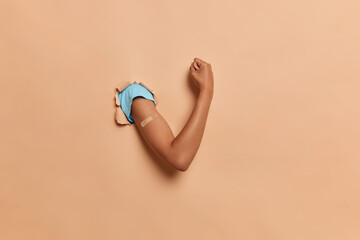 Thin nice female hand in blue tshirt breaks through the paper wall, shows muscles and compressed...
