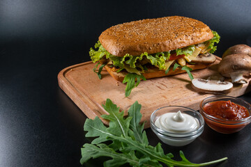 Fresh and tasty Italian panini, sandwich with ham and vegetables, sauce, salad, mushrooms, tomato and cucumber, on wooden spacing, plate. Black background