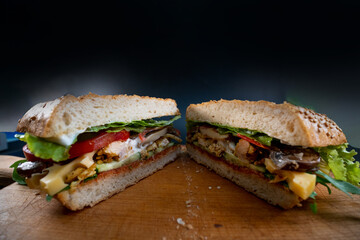 Fresh and tasty Italian panini with chicken and vegetables, sauce, salad, mushrooms, tomato and cucumber, on wooden spacing, plate. cut in half. Black background. Selective focus