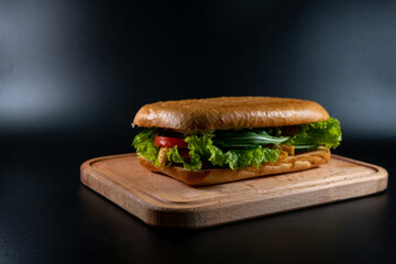 Fresh and tasty Italian panini, sandwich with chicken and vegetables, sauce, salad, mushrooms, tomato and cucumber, on wooden spacing, plate. Black background