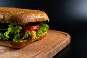 Fresh and tasty Italian panini, sandwich with ham and vegetables, sauce, salad, mushrooms, tomato and cucumber, on wooden spacing, plate. Black background
