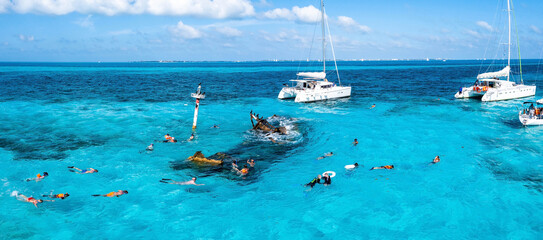 People snorkelling around the ship wreck near Bahamas in the Caribbean sea. Beautiful turquoise water with people swimming with fishes, aerial view.