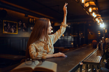 Woman with raised hand sitting at counter in bar