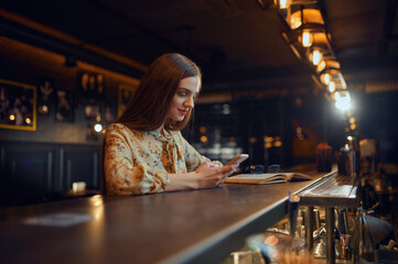 Woman with mobile phone sitting at counter in bar