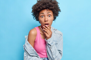 Fototapeta na wymiar Surprised pretty African American girl gets a big promotion, does not know how to react, raises her hand to her face shocked and her eyebrows. Tries to understand, wears a jeans jacket and a pink top