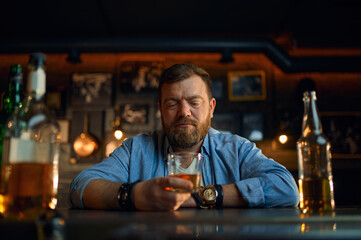 Serious man with glass of alcohol sitting in bar