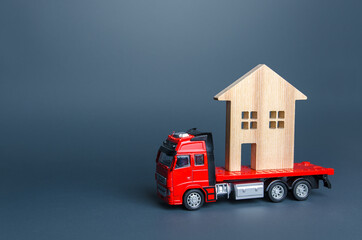 Fototapeta premium Red truck transports the residence house. Delivery services to another house. A moving company. Transportation of real estate. Resettlement program for new housing. Building insurance.