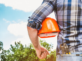 Attractive man in work clothes, holding construction helmet in his hands against the background of...