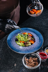 A professional chef prepares a delicious fresh salad of green vegetables and juicy veal in a modern and stylish restaurant. Cooking in a restaurant.