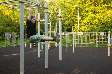 A guy does an exercise on a horizontal bar in the park. The concept of sports, fitness and a healthy lifestyle is a man performing an exercise on a horizontal bar on a sports field in a city park.