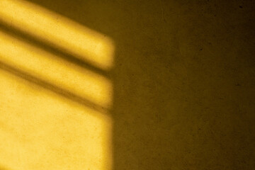 Abstract background with light and shadow falling on a dusty yellow wall.