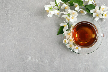 Glass cup of aromatic jasmine tea and fresh flowers on grey table, flat lay. Space for text