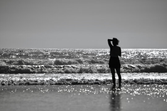 Silhouette images of surfers riding waves on Llangennith Beach on the Gower Peninsula. A popular sport for water sport activities with its sandy beach and rolling waves. Sun glistening on the water
