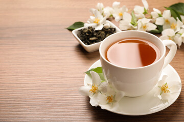 Cup of aromatic jasmine tea and fresh flowers on wooden table, space for text