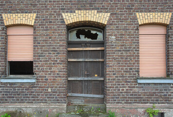 facade of an old brick house with windows and a blocked wooden door. brocken glass
