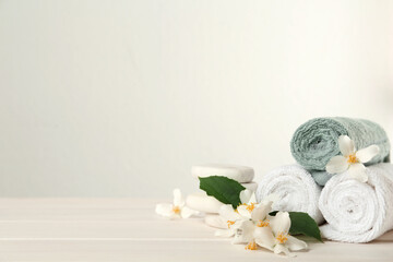 Beautiful jasmine flowers, spa stones and towels on white wooden table, space for text