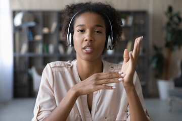 Fototapeta na wymiar Head shot portrait young African American woman in headphones speaking and looking at camera, confident mentor teacher recording webinar, explaining, businesswoman involved in internet negotiations