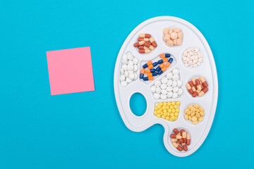 Global Pharmaceutical Industry and Medicinal Products - Different Colored Pills, Tablets and Capsules on White Art Palette with Blank Sticky Note and Copy Space Lying on Blue Background, Flat Lay