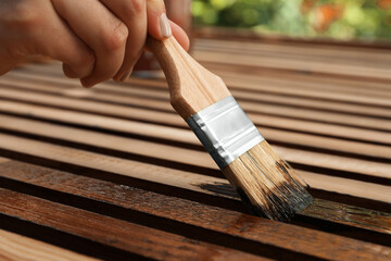 Woman applying wood stain onto planks outdoors, closeup