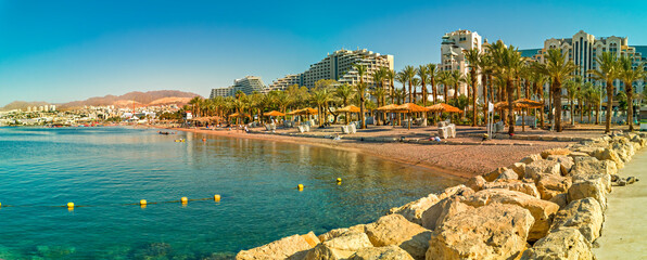 Swimming morning at sandy beach of the Red Sea, panoramic view from central stone walking pier and promenade in Eilat - famous tourist resort city in Israel 