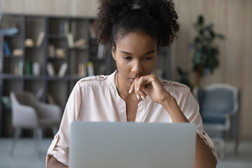 Close up thoughtful African American woman looking at laptop screen, focused pensive young businesswoman freelancer or student pondering strategy, working on research project, reading information