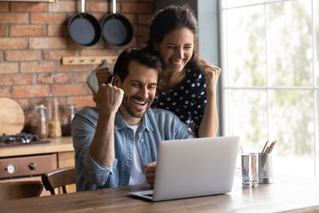 Happy excited young couple making winner yes hand fist gesture at laptop, getting awesome news,...