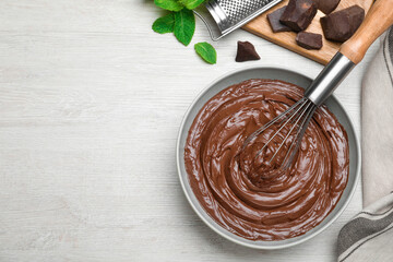 Chocolate cream with balloon whisk and mint on white wooden table, flat lay. Space for text