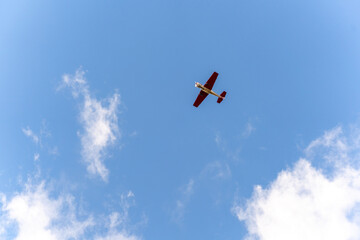 A small single-engine plane flies in the sky against a background of white clouds
