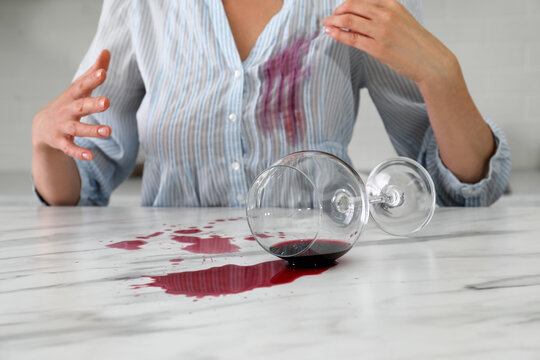 Woman with spilled glass of wine and stain on her shirt at table indoors, closeup