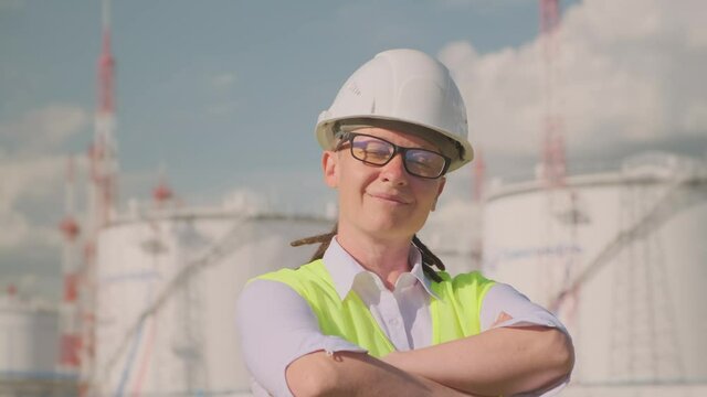 Portrait of successful woman employee of oil company on background of petroleum storage looking into camera.