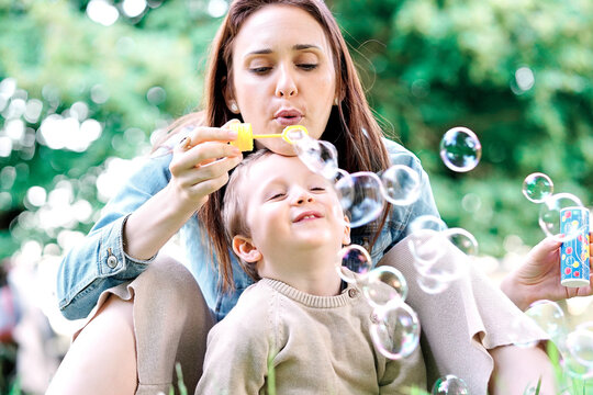 millennial mother with her three year old son blowing soap bubbles