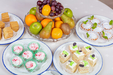 Four plates with different cakes. A bowl of fruit.